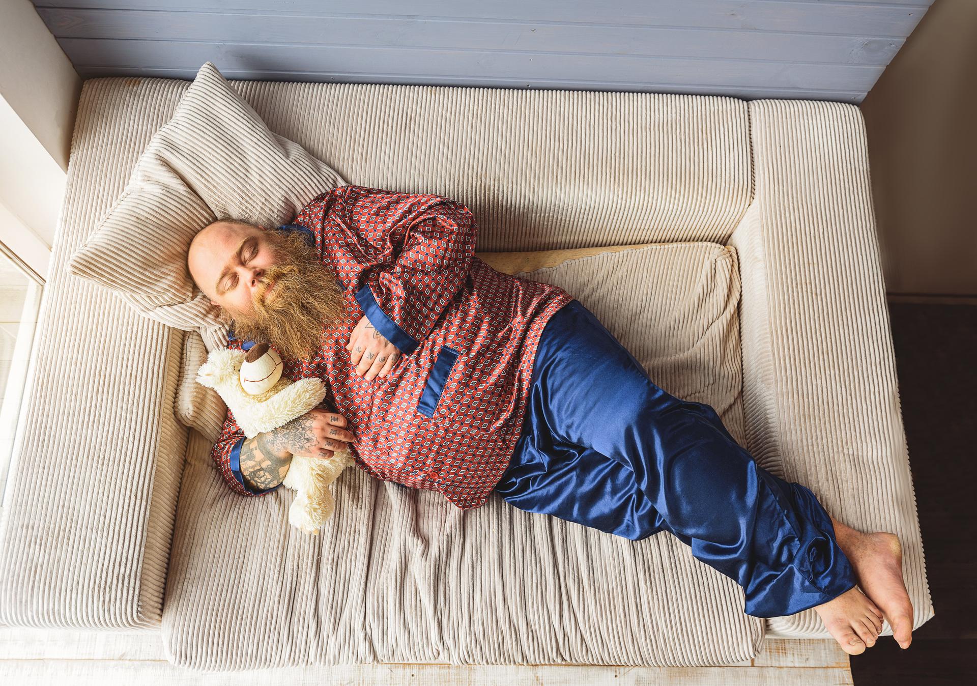 Sweet dreams. Innocent fat man is sleeping on sofa while hugging teddy bear