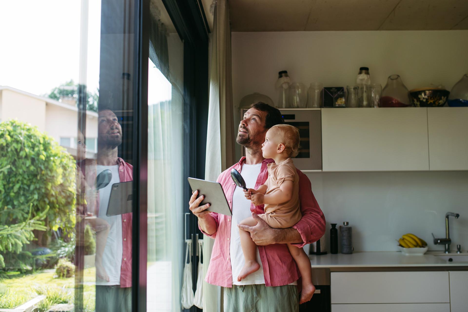 Man holding baby and closing metal blinds on smart home automation system. Smart home technology for sustainable living.