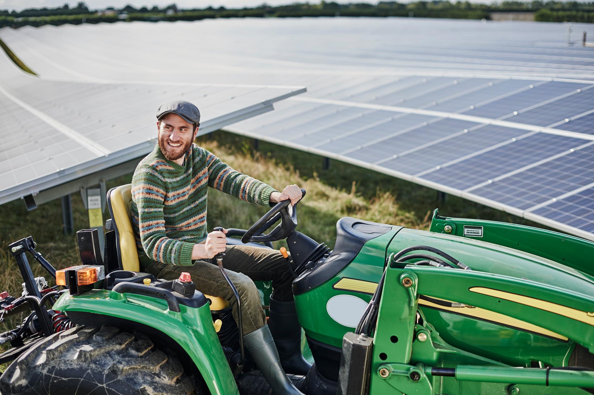 Agri PV Betreuung durch Bauer auf Traktor im PV-Feld, Photovoltaik, Landwirtschaftliche Nutzung, Traktor, Feld, Agrarwirtschaft