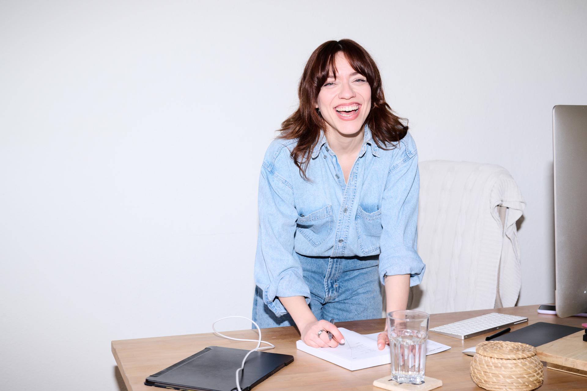 woman with a contagious smile, wearing a light blue denim shirt, laughs wholeheartedly