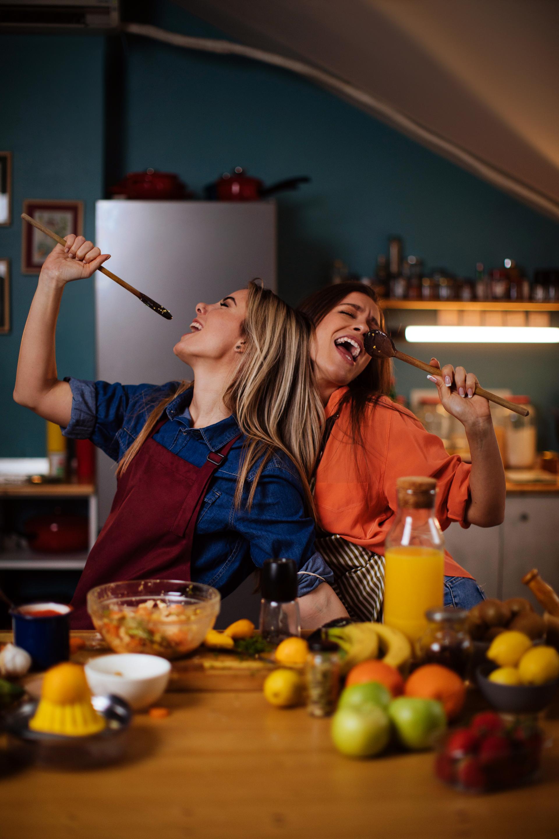 GettyImages-1378311399, Zwei Frauen singen in der Küche und kochen zusammen