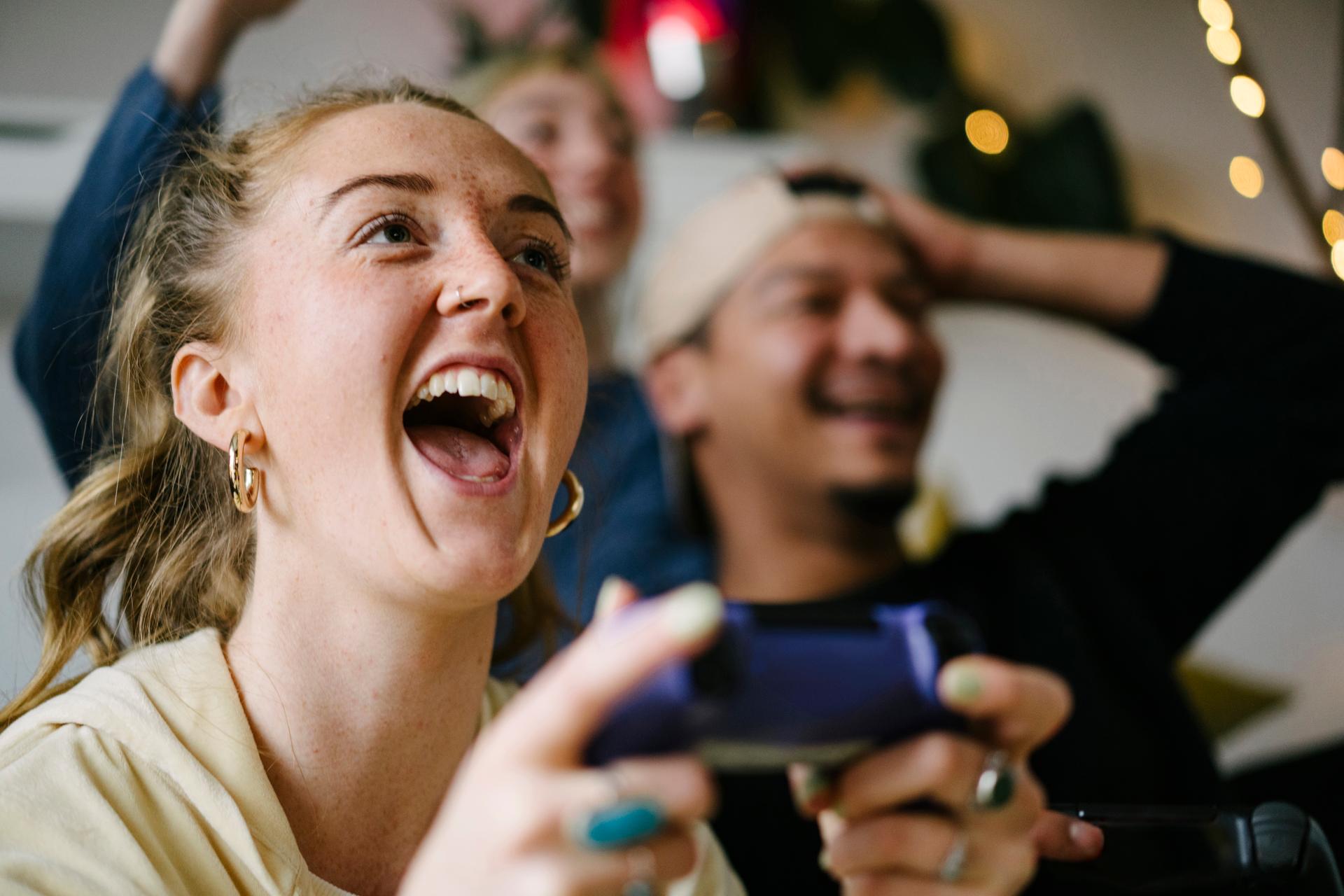View from below of a woman who is happy while playing with a controller, her friends can be seen blurred in the background